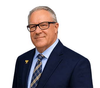 Professional headshot of Ron Skaggs wearing a navy suit, light blue dress shirt, patterned tie, and gold CASA lapel pin